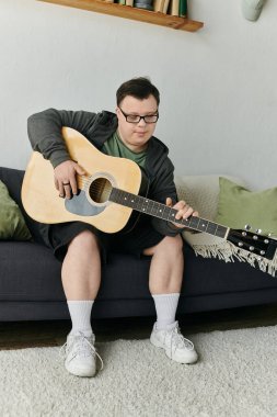 Down sendromlu bir adam koltukta dinlenirken gitarını neşeli bir şekilde tıngırdatır..
