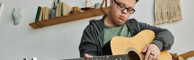 Down sendromlu genç adam sıcak ev dekoruyla çevrili gitar çalmayı seviyor..