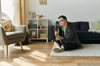 Down sendromlu genç bir adam gitar çalıyor, rahat bir oturma odasında müzik dinliyor..