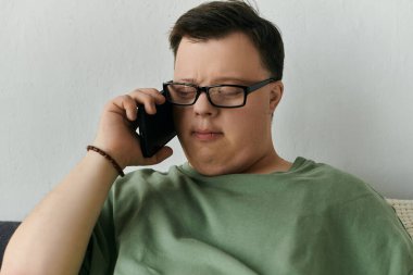 Down sendromlu bir adam evinde rahat bir şekilde otururken düşünceli bir telefon görüşmesi yapıyor..
