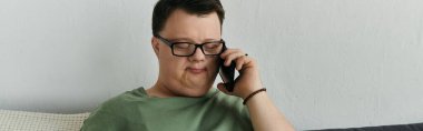 Down sendromlu bir adam telefonda konuşuyor, rahat yaşam alanında gülümsüyor..