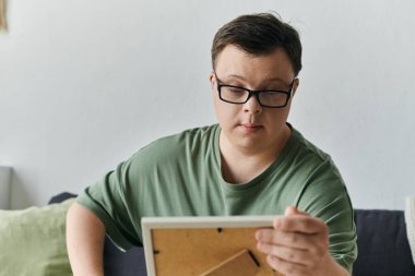 Down sendromlu genç bir adam yaşam alanında rahatça otururken sanat yaratıyor..