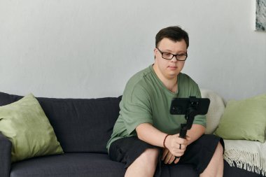 Down sendromlu bir adam kanepede dinlenirken video görüşmesinde neşeyle etkileşime geçer..