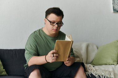 Down sendromlu genç bir adam rahat bir koltukta kitap okumaktan hoşlanır..