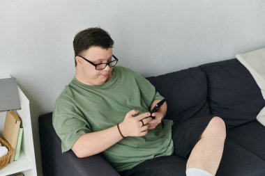 Down sendromlu bir adam evinde, kanepede rahat bir şekilde otururken akıllı telefonunun tadını çıkarıyor..