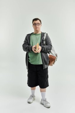 A young man with Down syndrome holds a book while standing comfortably at home.