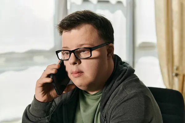 Stock image A young man with Down syndrome is focused on a phone conversation in a cozy home environment.