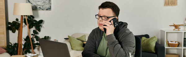 A young man with Down syndrome speaks on the phone while sitting at his desk.