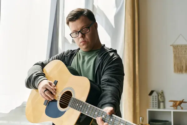 Stock image A young man with Down syndrome enjoys playing guitar in a cozy living space.