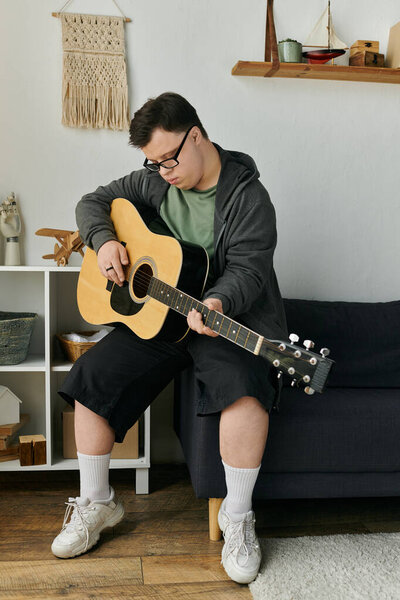 Молодой человек с синдромом Дауна задумчиво играет на гитаре в своем жилом пространстве..