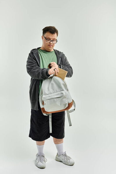 Молодой человек с синдромом Дауна готовит рюкзак в хорошо освещенной домашней обстановке..