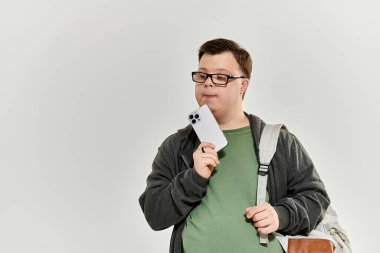 A young man with Down syndrome ponders while holding a smartphone at home.