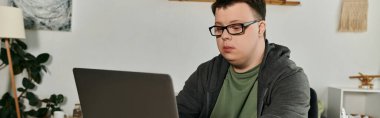 Down sendromlu genç bir adam rahat bir yaşam alanında laptopuna dikkatle odaklanır..