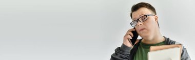 Down sendromlu bir adam elinde bazı dosyalar tutarken telefonla konuşuyor..
