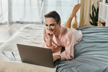 An enchanting drag queen relaxes on a bed while engaged with a laptop. clipart