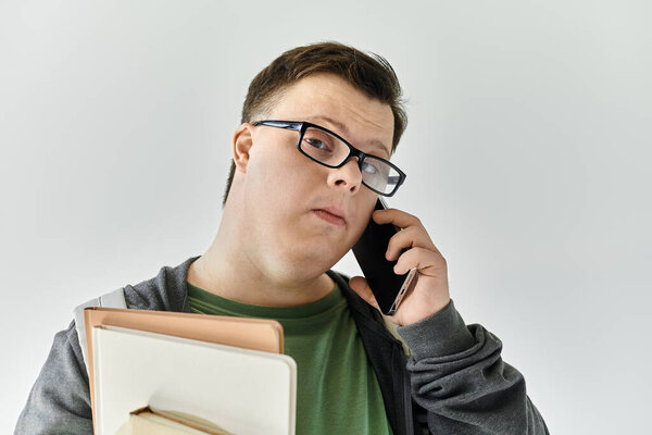 Молодой человек с синдромом Дауна разговаривает по телефону, держа папки.