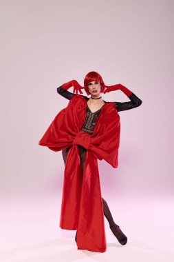 Çarpıcı bir travesti dikkat çekici kırmızı bir kıyafet ve sert bir poz sergiliyor..