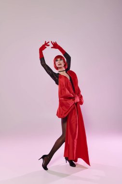 Çarpıcı travesti hareketli bir kırmızı elbiseyle dinamik bir poz veriyor..