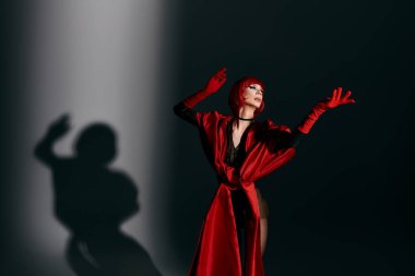 Büyüleyici bir travesti dramatik ışıklandırma altında canlı kıyafetler ve çarpıcı bir ifade sergiliyor..