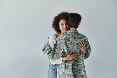 A soldier in camouflage uniform embraces her wife, capturing a moment of love and support before service. clipart