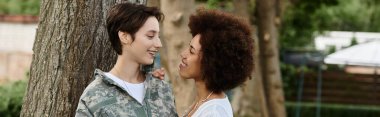 A joyful reunion as a female soldier in camouflage is warmly welcomed by her wife, celebrating love and home. clipart