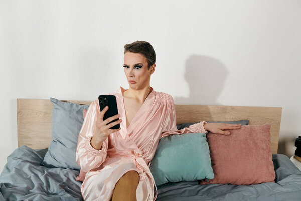 Attractive young drag queen relaxes on a bed while checking their phone.