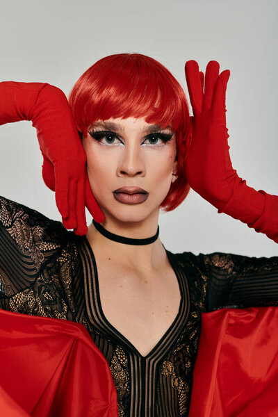 A stylish drag queen shows off bold makeup and vibrant red attire.