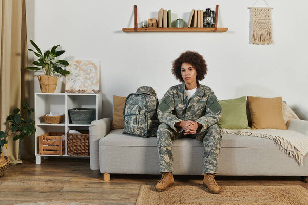Молодая афроамериканка в военном снаряжении сидит задумчиво в своей гостиной, готовая к развертыванию.