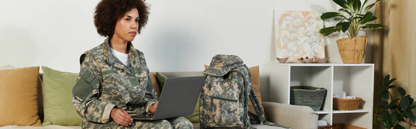 A dedicated young military woman studies on a laptop while seated comfortably in a cozy, modern interior.