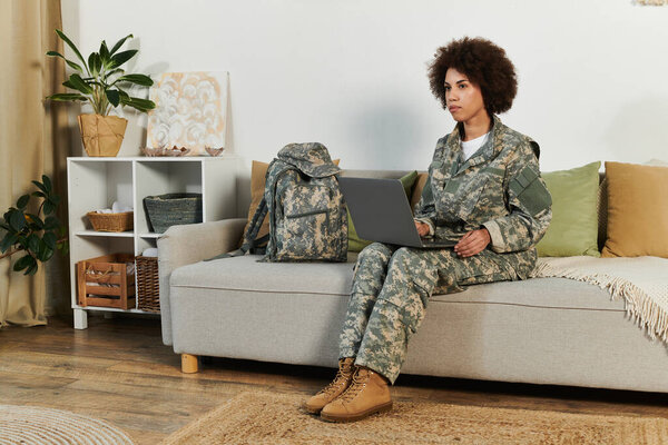 A young African American woman in military attire focuses on her laptop, balancing duty and home life.