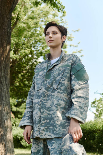 Молодой военный в камуфляже с гордостью стоит на улице, наслаждаясь моментом возвращения домой.