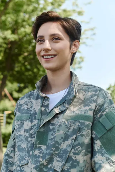 Stock image A young woman in camouflage smiles brightly, celebrating her homecoming in the warm sunlight.