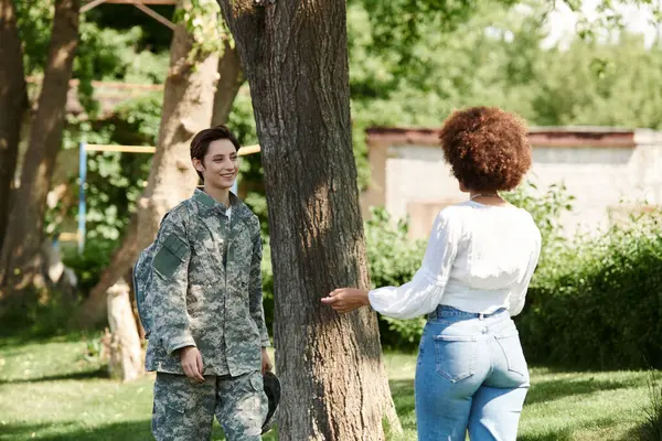 stock image A joyful reunion unfolds as a soldier greets her wife beneath the shade of a tree.