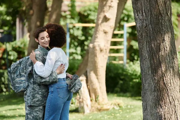 stock image A joyous reunion unfolds as a soldier in uniform embraces her loving wife in a serene park.