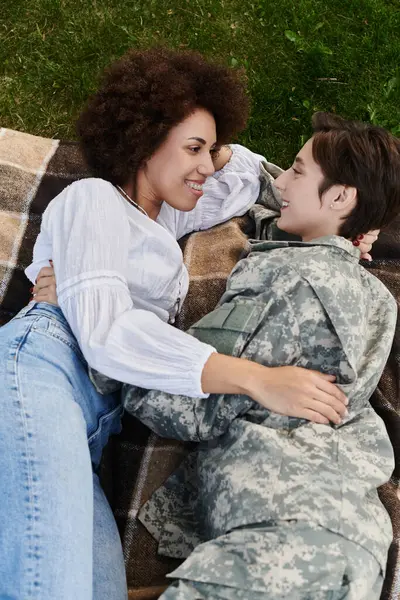 stock image A soldier in camouflage reunites with her wife, sharing a tender moment on a cozy blanket.