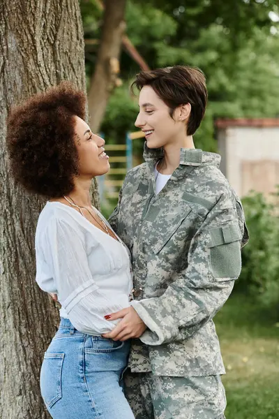 Stock image A young female soldier in camouflage shares a heartfelt reunion with her wife in a vibrant outdoor setting.