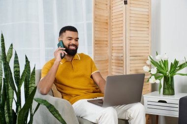 Bir adam evde dizüstü bilgisayarı üzerinde çalışırken bir telefon görüşmesi yapar..
