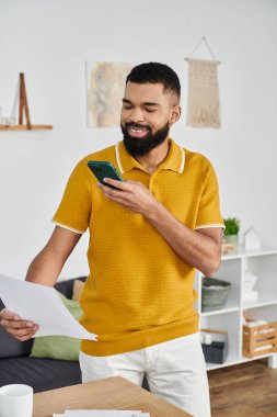 Gülümseyen bir adam akıllı telefonunu kullanırken belgelere göz atar..
