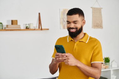 Gülümseyen adam telefonunu kontrol ediyor, evde bir anlık rahatlamaya dalmış..