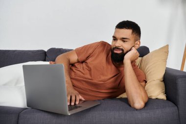 Evde uzanıp laptopuyla rahatça meşgul olan yakışıklı bir adam..