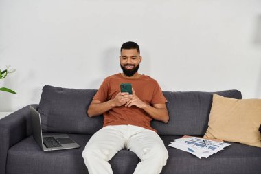 Adam rahat bir ev ortamında uzanırken mutlu bir şekilde akıllı telefon kullanıyor..