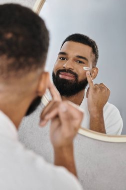 Bir erkek, yansımasına gülümserken cilt bakımını sever..