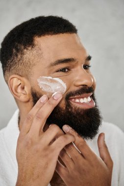 Bir adam evde eğlenirken gülümseyerek nemlendirici sürer..