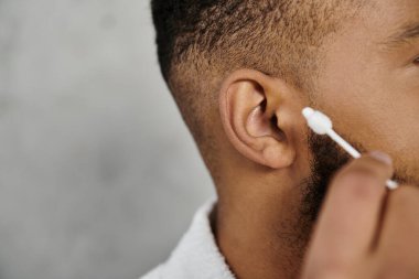 Man carefully grooming his beard with a cotton swab at home. clipart