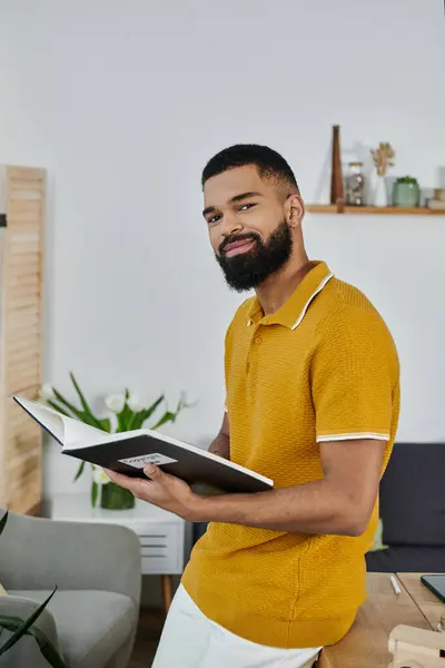 stock image A stylish man smiles while reading a book in a tranquil home environment.