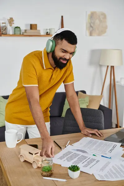 stock image A cheerful man engages in projects at home, immersed in creative tasks with headphones.