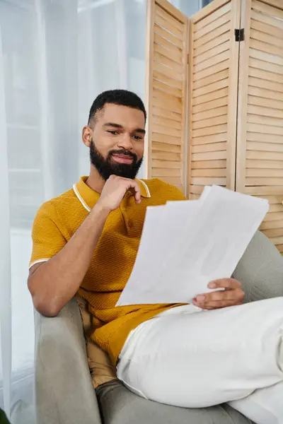 stock image A handsome man attentively reviews papers while lounging at home.