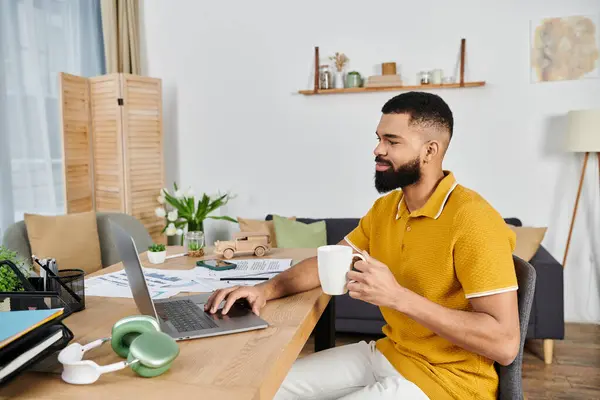 stock image A man sips coffee and works on his laptop in a warm, inviting space.