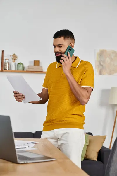 stock image A stylish man chats on the phone while reviewing documents at home.