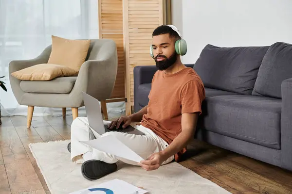 stock image A man sits comfortably on the floor, focused on his laptop with headphones on.